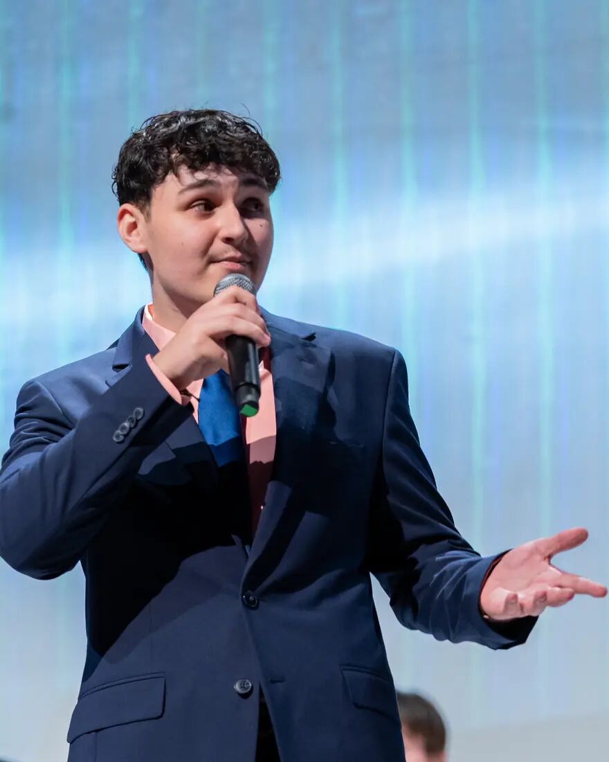 Cooper Bailey speaking into a microphone on stage with ReScored A Cappella